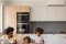 The image shows a young father with his two daughters in a kitchen, with the indoor unit of a Carrier air conditioning system on the wall.